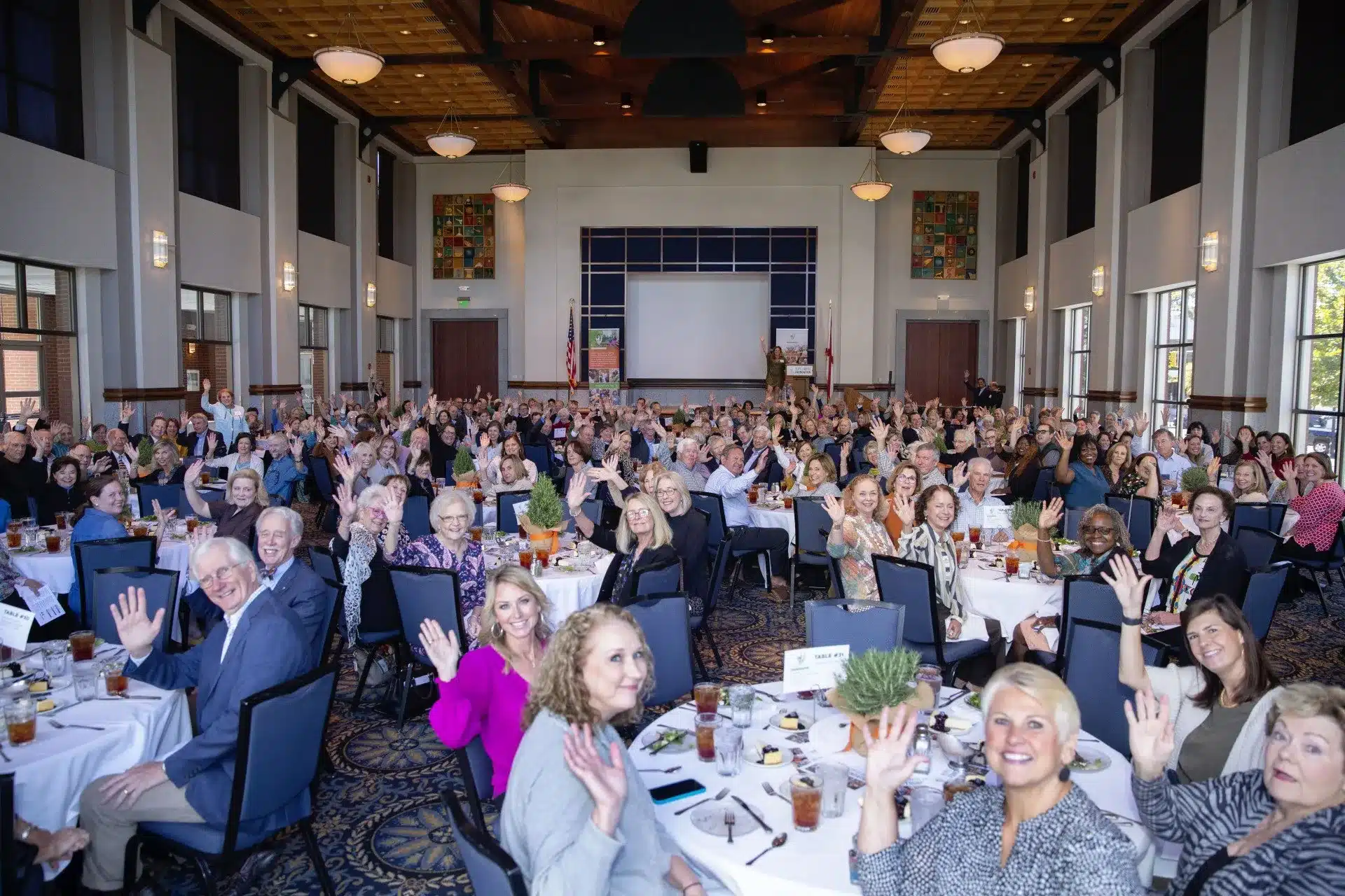 Large group of people, smiling and waving at the camera during the Respite for All Brain Science Luncheon event.
