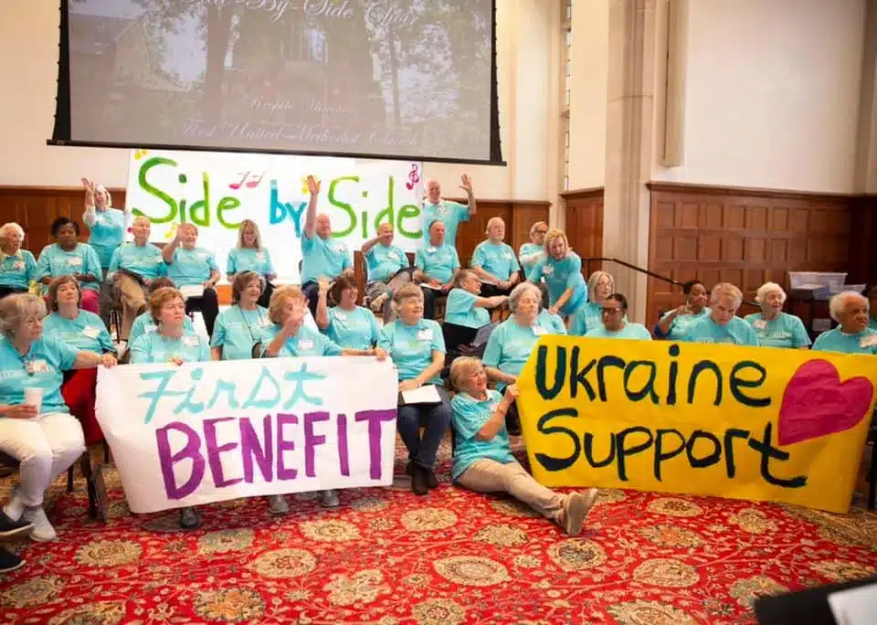 A group of volunteers pose in a church with banners reading "First Benefit" and "Ukraine Support," celebrating a choir benefit concert.