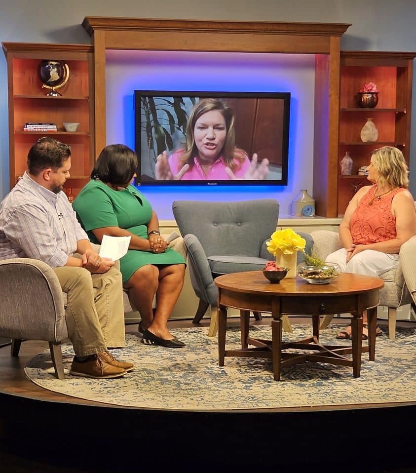 News interview set with three people seated, watching Daphne Johnston on a screen discussing caregiver well-being.