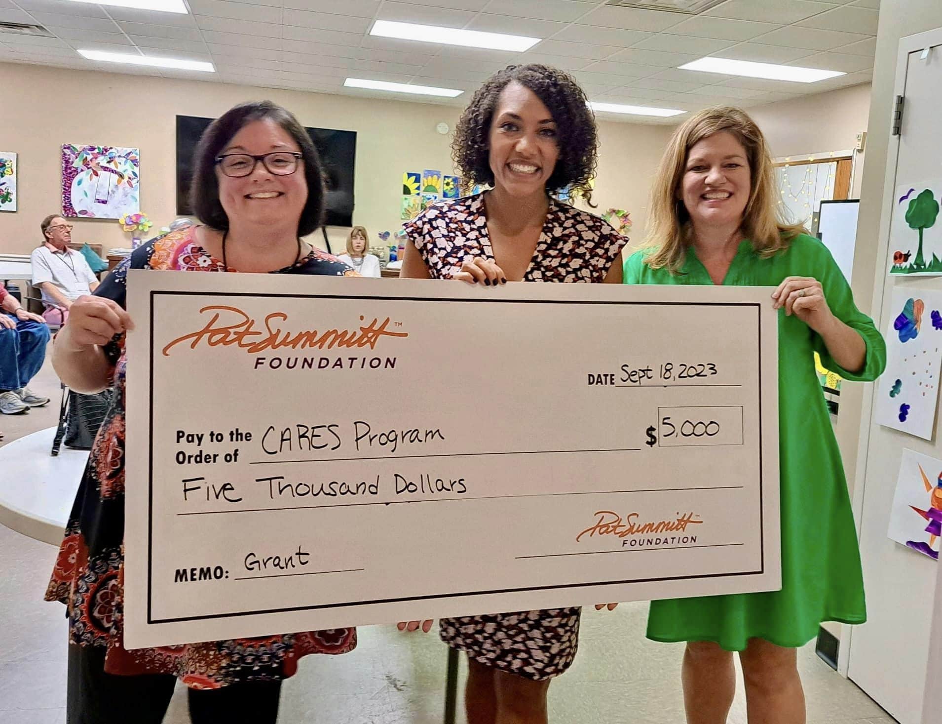 Three smiling women hold a large $5,000 check from the Pat Summitt Foundation for the CARES Program at a Respite For All event.