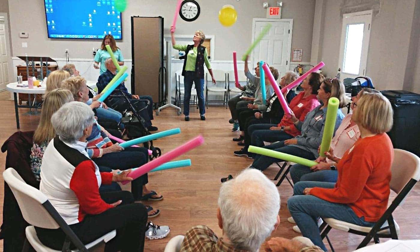 Respite for All friends sit in a row facing each other keeping balloons in the air with pool noodles.