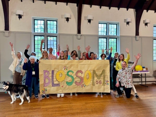 Blossom opening A group of volunteers and participants smiling and waving in front of a large "BLOSSOM" banner at The Blossom event at St. John's Episcopal Church.